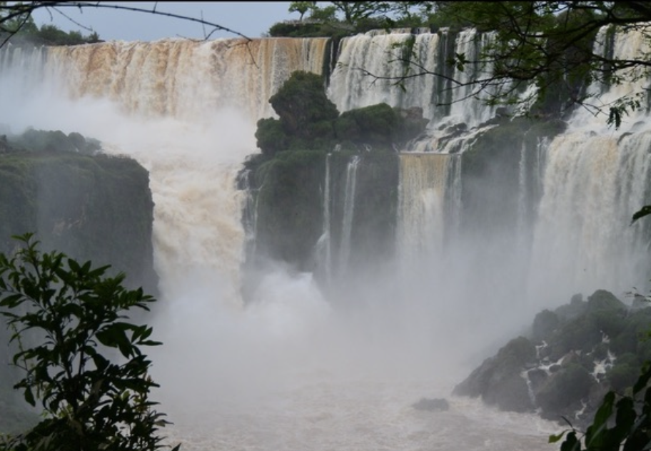 A broad waterfall dropping into mist between rocks and trees